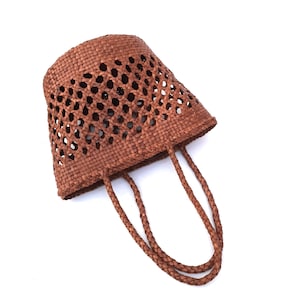 May include: A brown woven tote bag with a unique open weave design. The bag features two braided handles and a tapered shape. The bag is made of a natural material and is suitable for carrying items.