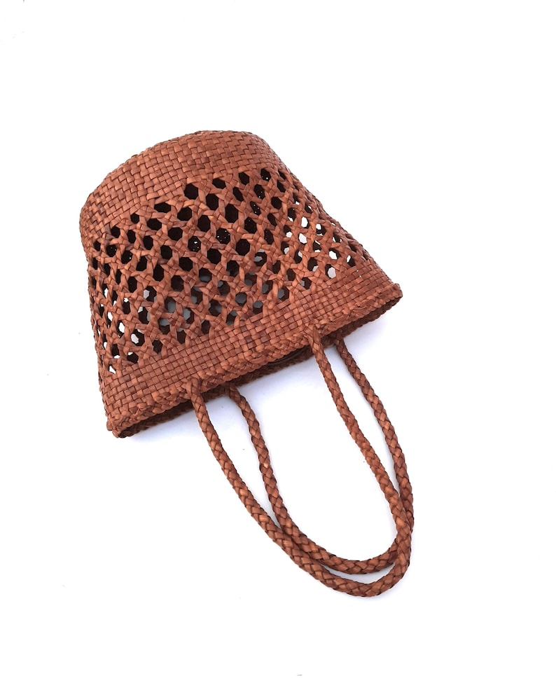 May include: A brown woven tote bag with a unique open weave design. The bag features two braided handles and a tapered shape. The bag is made of a natural material and is suitable for carrying items.