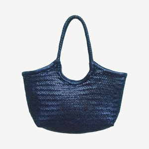 May include: A navy blue woven tote bag with a braided handle. The bag has a rounded shape with a wide opening and a textured, basket-weave pattern. The handle is arched and attached to the top of the bag.