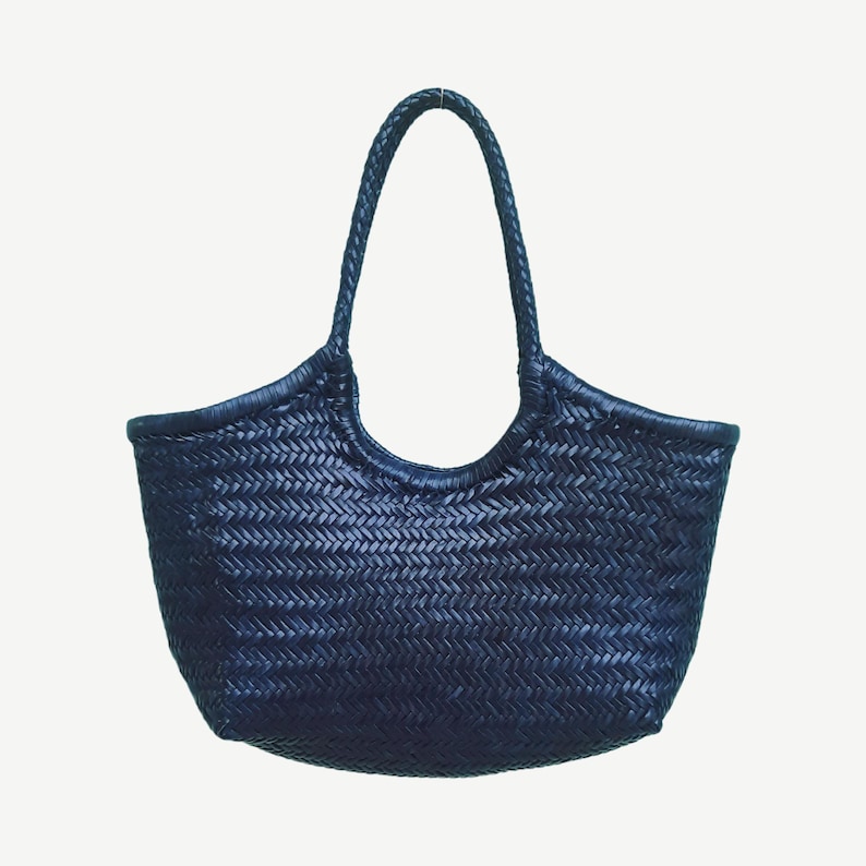 May include: A navy blue woven tote bag with a braided handle. The bag has a rounded shape with a wide opening and a textured, basket-weave pattern. The handle is arched and attached to the top of the bag.