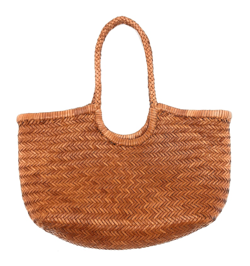May include: A woven brown tote bag with a braided handle. The bag has a rounded shape and a textured surface created by the woven pattern. The handle is arched and attached to the top of the bag.