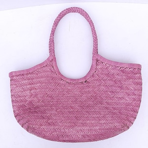 May include: A woven pink tote bag with a braided handle. The bag has a rounded shape with a wide opening and a textured, basket-like weave. The handle is a thick, braided design, and the bag is made of a natural material.
