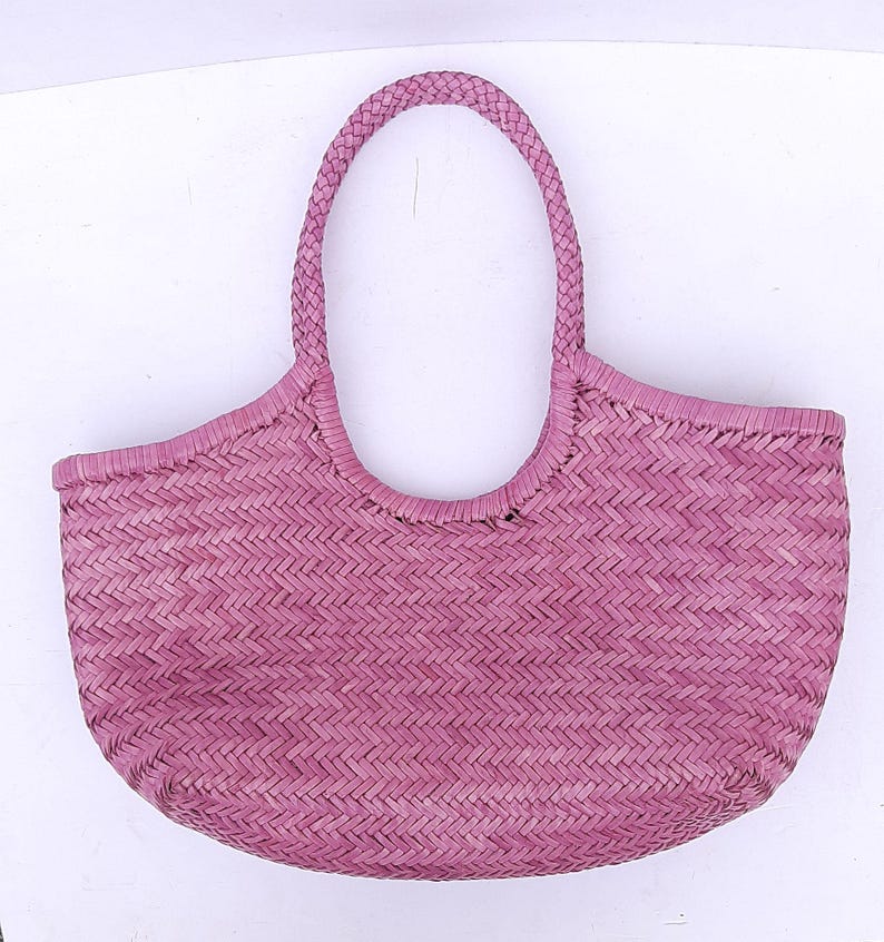 May include: A woven pink tote bag with a braided handle. The bag has a rounded shape with a wide opening and a textured, basket-like weave. The handle is a thick, braided design, and the bag is made of a natural material.