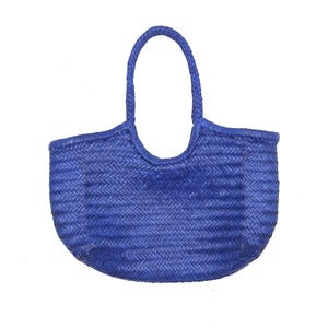 May include: A woven blue tote bag with a single braided handle. The bag has a rounded shape and a textured surface, suitable for carrying items. The bag is made of a durable material.