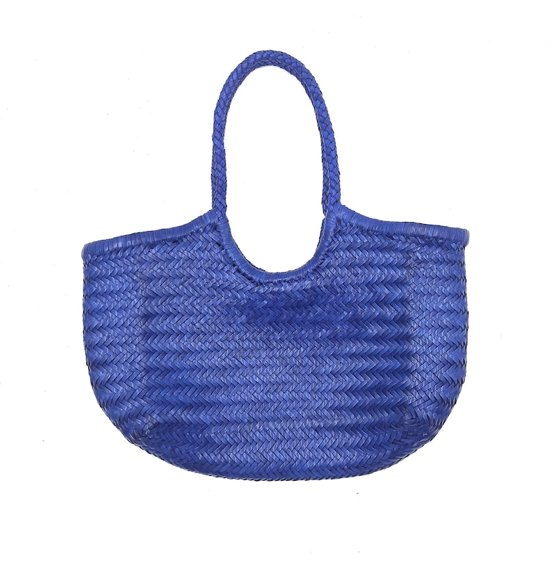 May include: A woven blue tote bag with a single braided handle. The bag has a rounded shape and a textured surface, suitable for carrying items. The bag is made of a durable material.