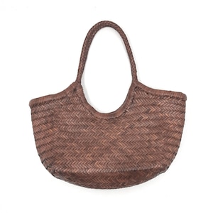May include: A brown woven tote bag with a rounded base and a braided handle. The bag has a basket-like appearance, with a textured surface and a sturdy design. The handle is arched, and the bag is set against a white background.