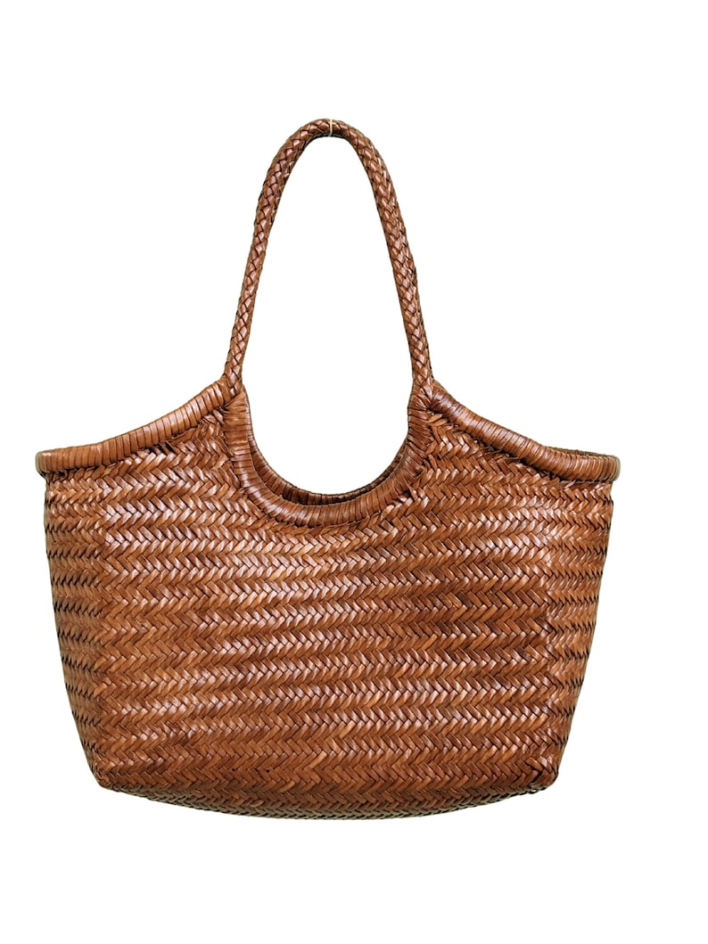 May include: A woven brown tote bag with a braided handle. The bag has a rectangular shape with rounded corners and a wide opening. The weave pattern is visible throughout the bag's body and handle.