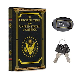 May include: A black book-shaped safe with gold lettering that reads The Constitution of the United States of America, featuring a gold eagle emblem, a three-digit combination lock, and two silver metal keys on a ring for security access.