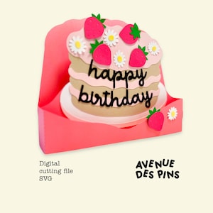 May include: A layered paper cake with pink frosting, strawberries, and daisies, with the words "happy birthday" in black script. The cake sits in a pink card holder. The image also includes the text "Digital cutting file SVG" and the logo "AVENUE DES PINS".