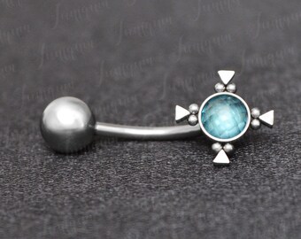 May include: Silver body piercing with a blue gem in the center of a cross design.