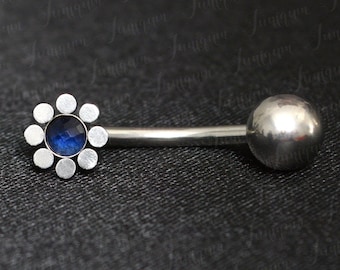 May include: A silver belly button ring with a blue gem in the center of a flower-shaped design.