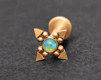 May include: Gold body jewelry with a green opal gemstone in the center. The jewelry is in the shape of a four-pointed star with small gold beads around the gemstone.