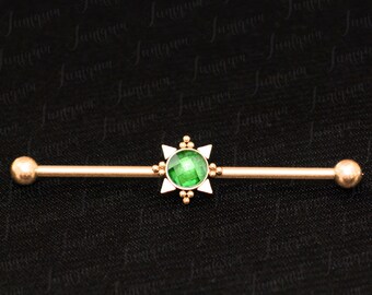 Puede incluir: Barbell de oro con una gema verde engastada en un diseño en forma de estrella. El barbell es una joya de piercing corporal.