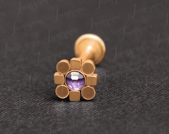 May include: Gold body jewelry with a purple gem in the center of a square design.