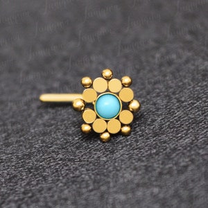 May include: Gold nose ring with a turquoise stone in the center and a circular design around it.
