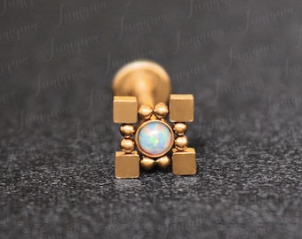 May include: Gold body jewelry with a square design and a small opal gemstone in the center.