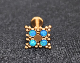 May include: Gold body jewelry with a square design featuring four blue opal stones. The jewelry is made of surgical steel and is suitable for a variety of piercings.