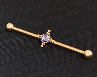 Puede incluir: Barbell de oro con una gema púrpura y un diseño geométrico. La barra es de acero quirúrgico y es adecuada para piercings corporales.