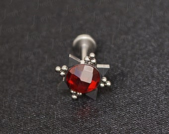 May include: A red gemstone set in a silver star-shaped setting. The gemstone is surrounded by small silver beads. The setting is attached to a silver post.