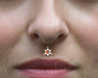 May include: Close-up of a person's face with a small gold star-shaped nose piercing with a red gem in the center.