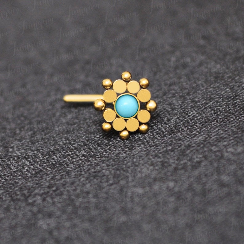 May include: Gold nose ring with a turquoise stone in the center and a circular design around it.