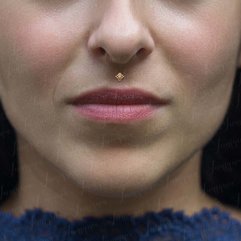 Op de afbeelding: Close-up van het onderste deel van het gezicht van een persoon met een kleine gouden oorbelpiercing in de onderlip.