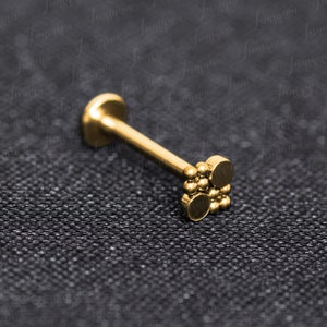 Op de afbeelding: Gouden lichaamsieraad met een kleine cluster van ronde kralen aan het uiteinde. De sieraden zijn gemaakt van chirurgisch staal en geschikt voor verschillende piercings.