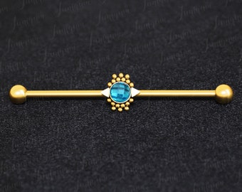 Puede incluir: Barbell de oro con una gema azul y detalles dorados. El barbell está sobre un fondo negro.