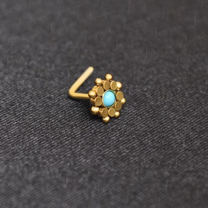 May include: Gold nose ring with a turquoise stone set in a circular design.