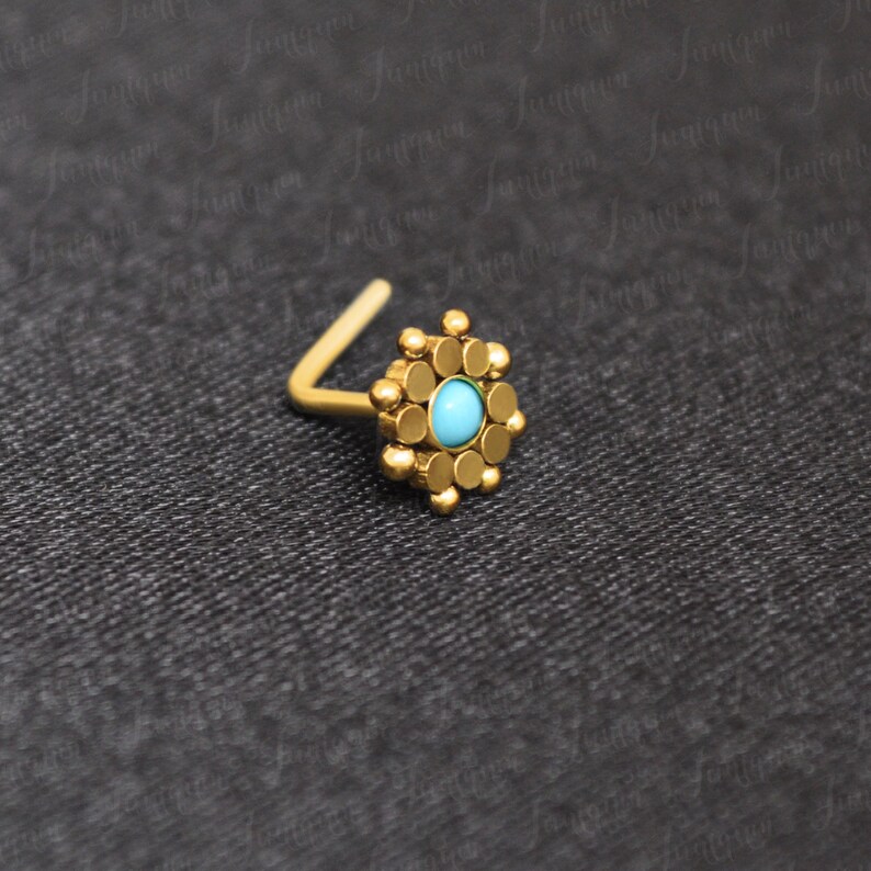 May include: Gold nose ring with a turquoise stone set in a circular design.