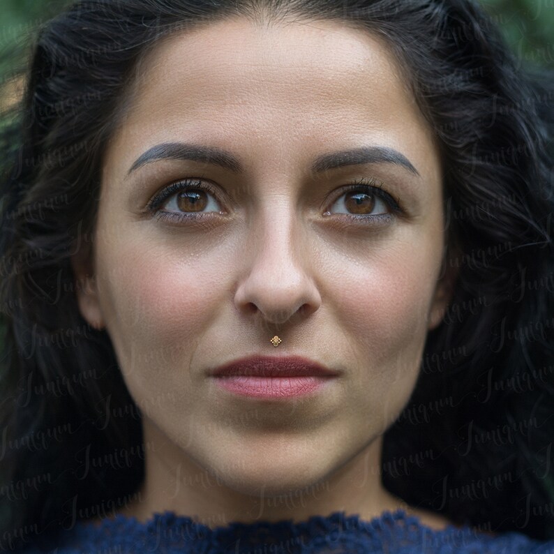 Op de afbeelding: Close-up portret van een persoon met donker haar en bruine ogen. Ze heeft een kleine gouden noppenpiercing in haar onderlip.