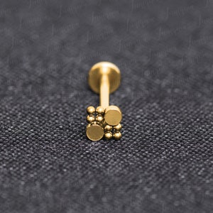 Op de afbeelding: Gouden lichaamsieraad met een klein, vierkant ontwerp met meerdere kleine balletjes. De sieraden zijn gemaakt van chirurgisch staal en geschikt voor verschillende piercings.