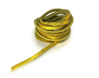 May include: Coiled gold-colored leather cord against a white background. The cord appears to be flat and textured, with a metallic sheen. The cord is likely used for jewelry making or crafts.