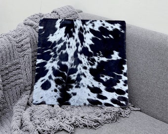 May include: A black and white cowhide patterned throw pillow on a gray couch.