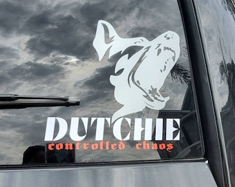 May include: A white silhouette of a dog with its mouth open, on a black car window. The text "DUTCHIE controlled chaos" is below the dog.