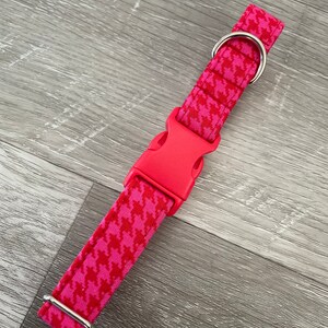 K&ouml;nnte beinhalten: Ein pinkfarbenes Hundehalsband mit Hahnentrittmuster und einer silbernen Schnalle und einem Ring.