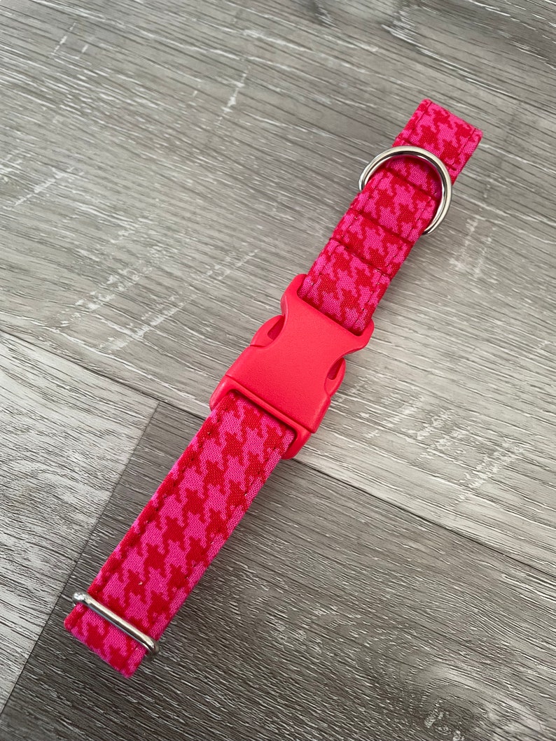 K&ouml;nnte beinhalten: Ein pinkfarbenes Hundehalsband mit Hahnentrittmuster und einer silbernen Schnalle und einem Ring.