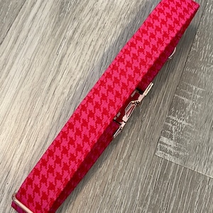 K&ouml;nnte beinhalten: Ein pinkfarbenes und wei&szlig;es Hundehalsband mit Hahnentrittmuster und ros&eacute;goldenen Beschl&auml;gen.