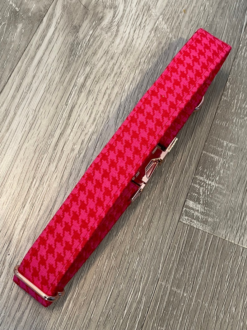 K&ouml;nnte beinhalten: Ein pinkfarbenes und wei&szlig;es Hundehalsband mit Hahnentrittmuster und ros&eacute;goldenen Beschl&auml;gen.