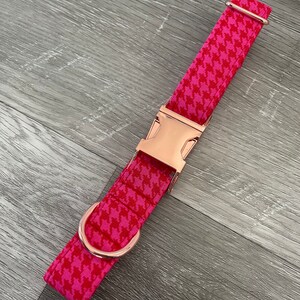 K&ouml;nnte beinhalten: Ein pinkfarbenes und wei&szlig;es Hundehalsband mit Hahnentrittmuster, einer ros&eacute;goldenen Schnalle und einem D-Ring.