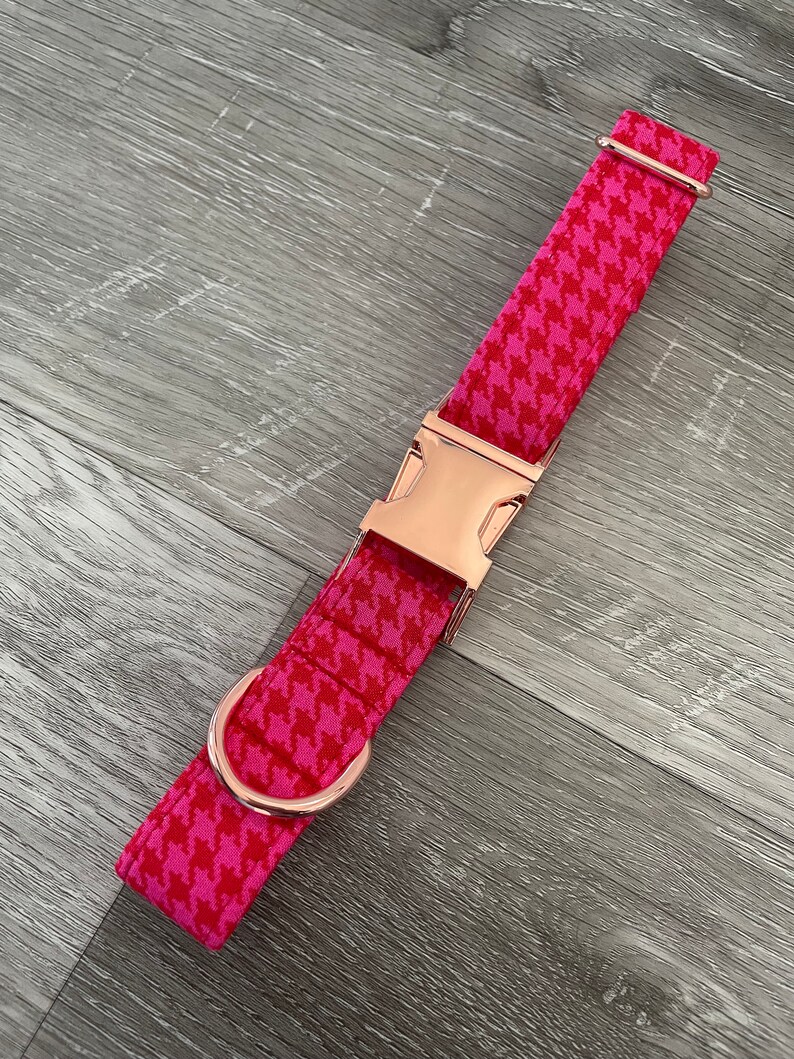 K&ouml;nnte beinhalten: Ein pinkfarbenes und wei&szlig;es Hundehalsband mit Hahnentrittmuster, einer ros&eacute;goldenen Schnalle und einem D-Ring.