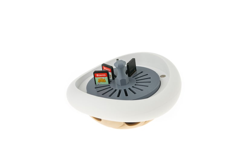 May include: White and gray game cartridge holder with a rotating carousel. The carousel has slots for multiple game cartridges. The holder is shaped like a mushroom.