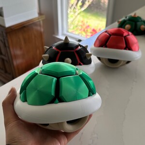 May include: Three 3D printed turtle shells, one green, one red, and one black with red accents. The shells are all in the shape of a turtle shell with a white base.