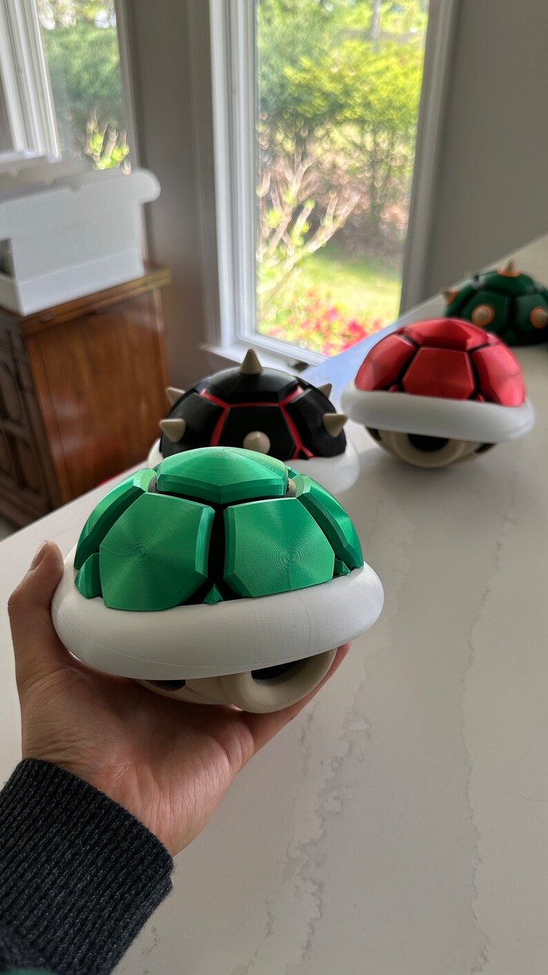May include: Three 3D printed turtle shells, one green, one red, and one black with red accents. The shells are all in the shape of a turtle shell with a white base.