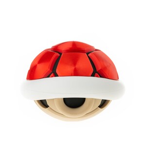 May include: A red and white shell-shaped toy with a black center. The toy is a replica of a popular video game item.