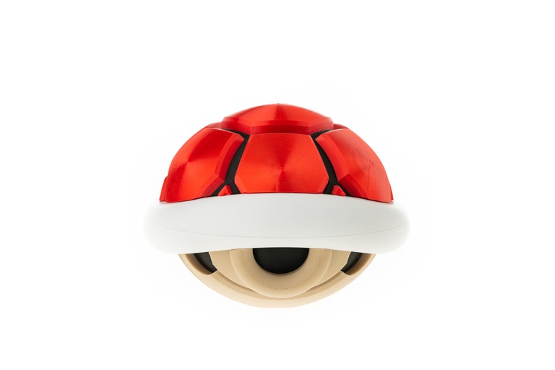 May include: A red and white shell-shaped toy with a black center. The toy is a replica of a popular video game item.
