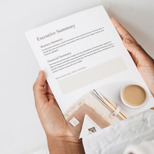 May include: A white sheet of paper with the text "Executive Summary" at the top. The text is divided into two sections: "Business Summary" and "Financial Summary". The text describes the importance of a business plan and financial summary. The paper is held by a person's hands.