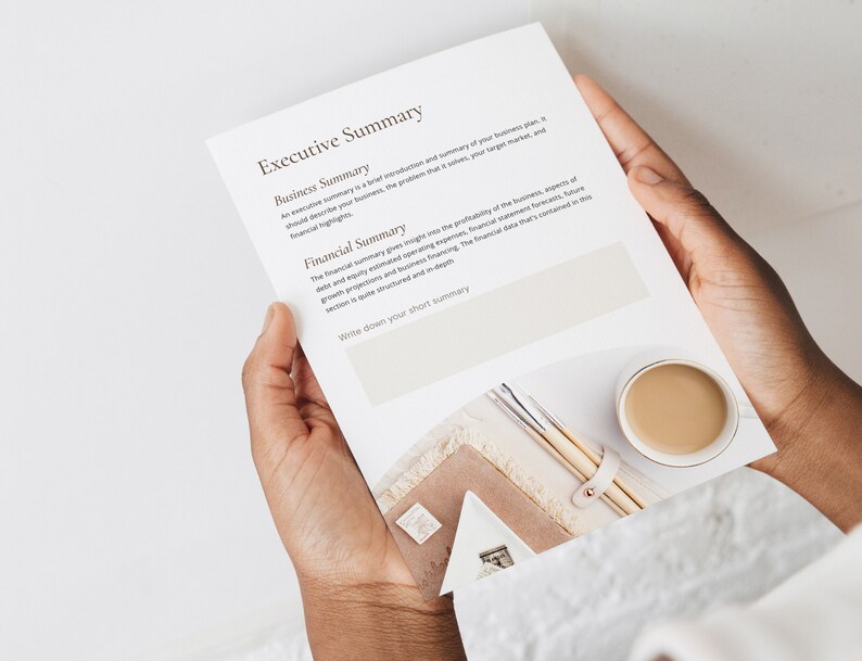 May include: A white sheet of paper with the text "Executive Summary" at the top. The text is divided into two sections: "Business Summary" and "Financial Summary". The text describes the importance of a business plan and financial summary. The paper is held by a person's hands.