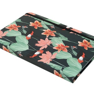 May include: A black notebook with a floral design featuring pink and orange flowers, green leaves, and black birds. The notebook has a black elastic closure.