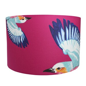 Puede incluir: Una pantalla de l&aacute;mpara rosa con un dise&ntilde;o de p&aacute;jaro azul y blanco. Los p&aacute;jaros est&aacute;n volando y tienen alas detalladas.